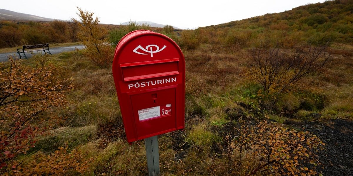 A red mailbox stands outdoors amidst autumn scenery.