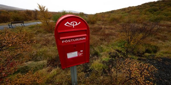 A red mailbox stands outdoors amidst autumn scenery.